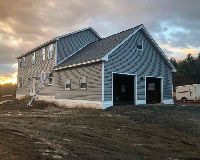 Two-story custom home with attached two-car garage built by Level Headed Builders in Springfield VT featuring grey horizontal siding