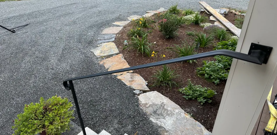 Custom home entryway and hardscaping by Level Headed Builders in Springfield VT with stone steps, handrail, and garden bed